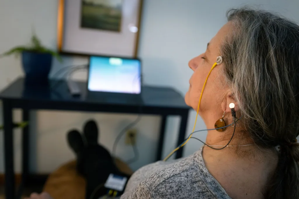 Woman with eyes closed and sensors on her scalp and ears, a laptop behind her
