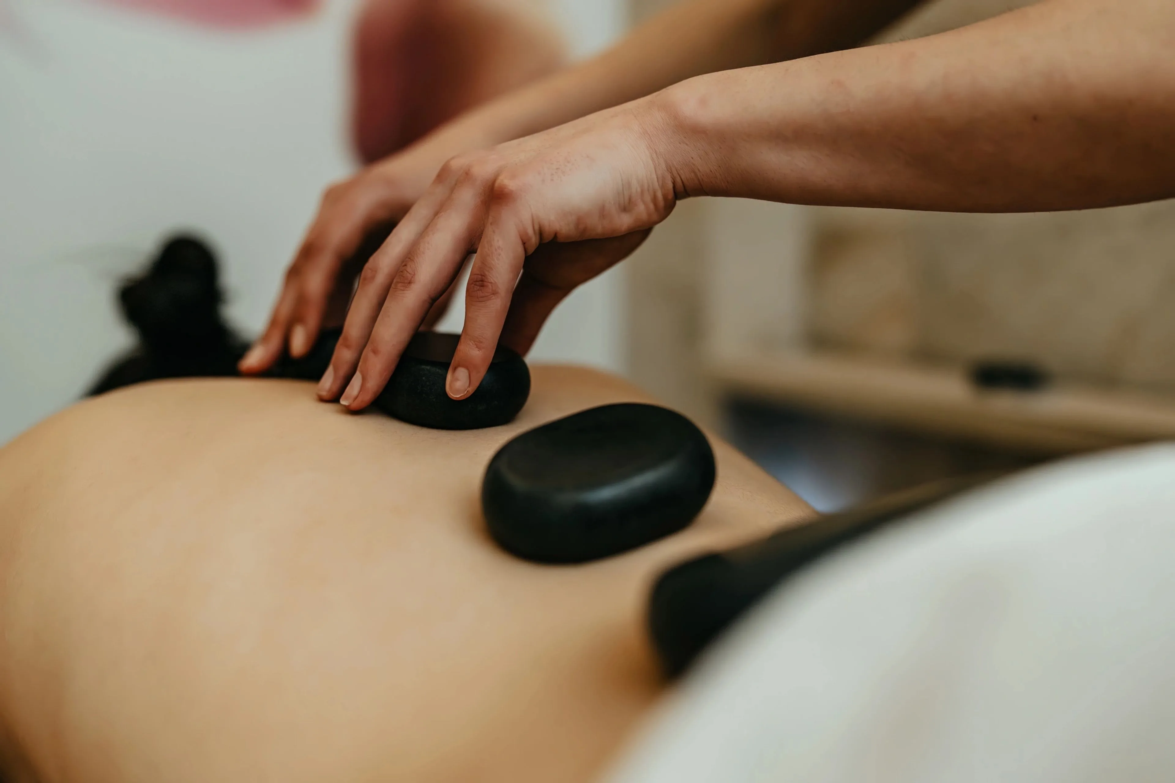 Therapist placing smooth black hot stones along a client's back during a massage