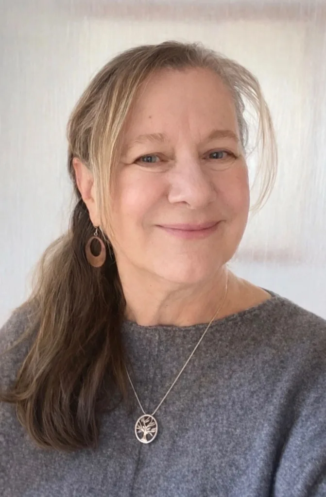 Smiling woman with long hair in a ponytail, wearing a gray sweater and jewelry.