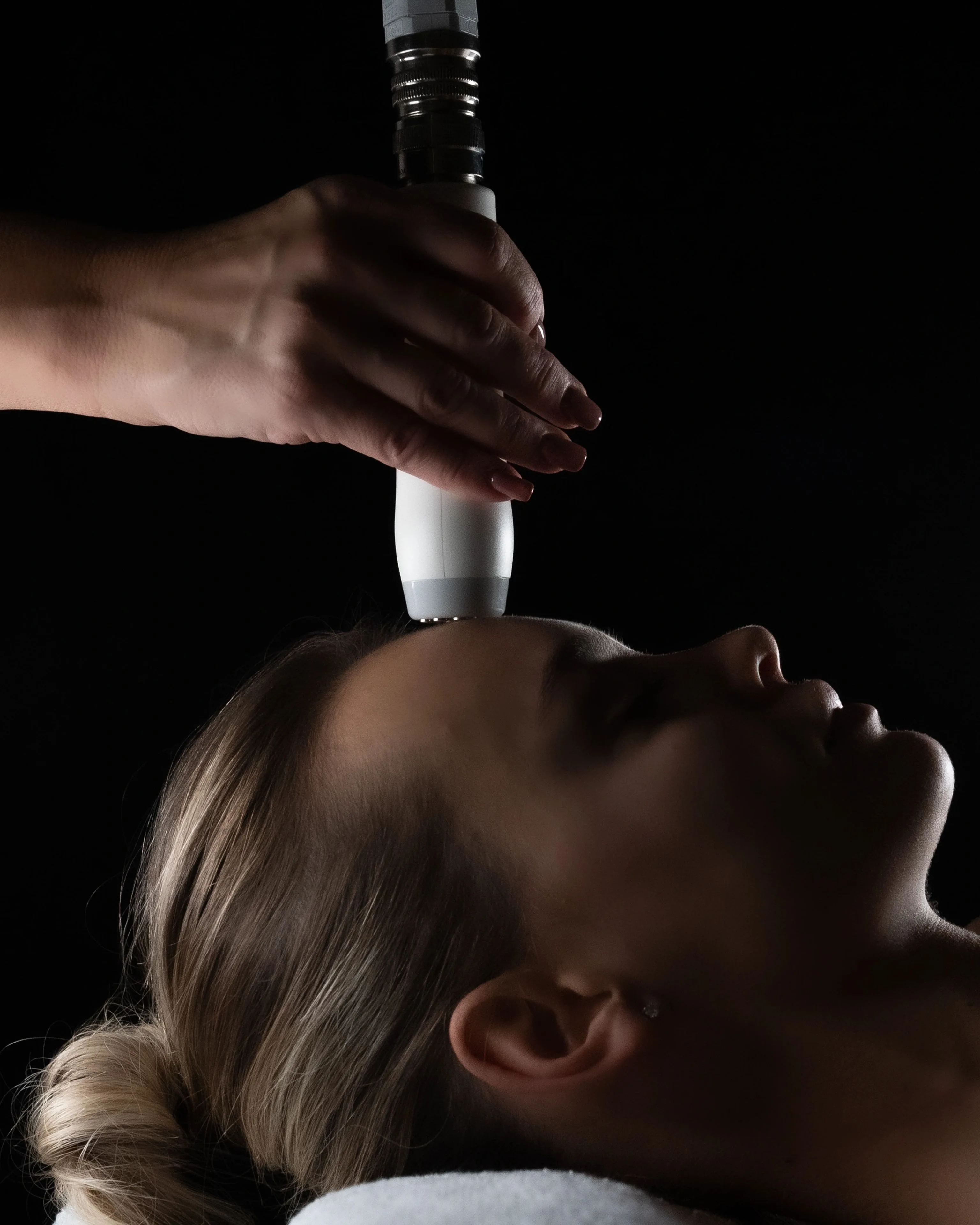 Treatment handpiece held above a reclining woman's forehead