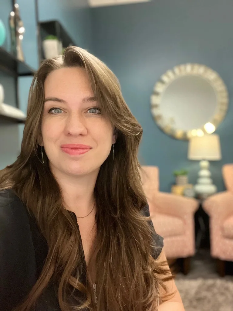 Hannah Sholar, life coach, smiling in an office with a round mirror behind her