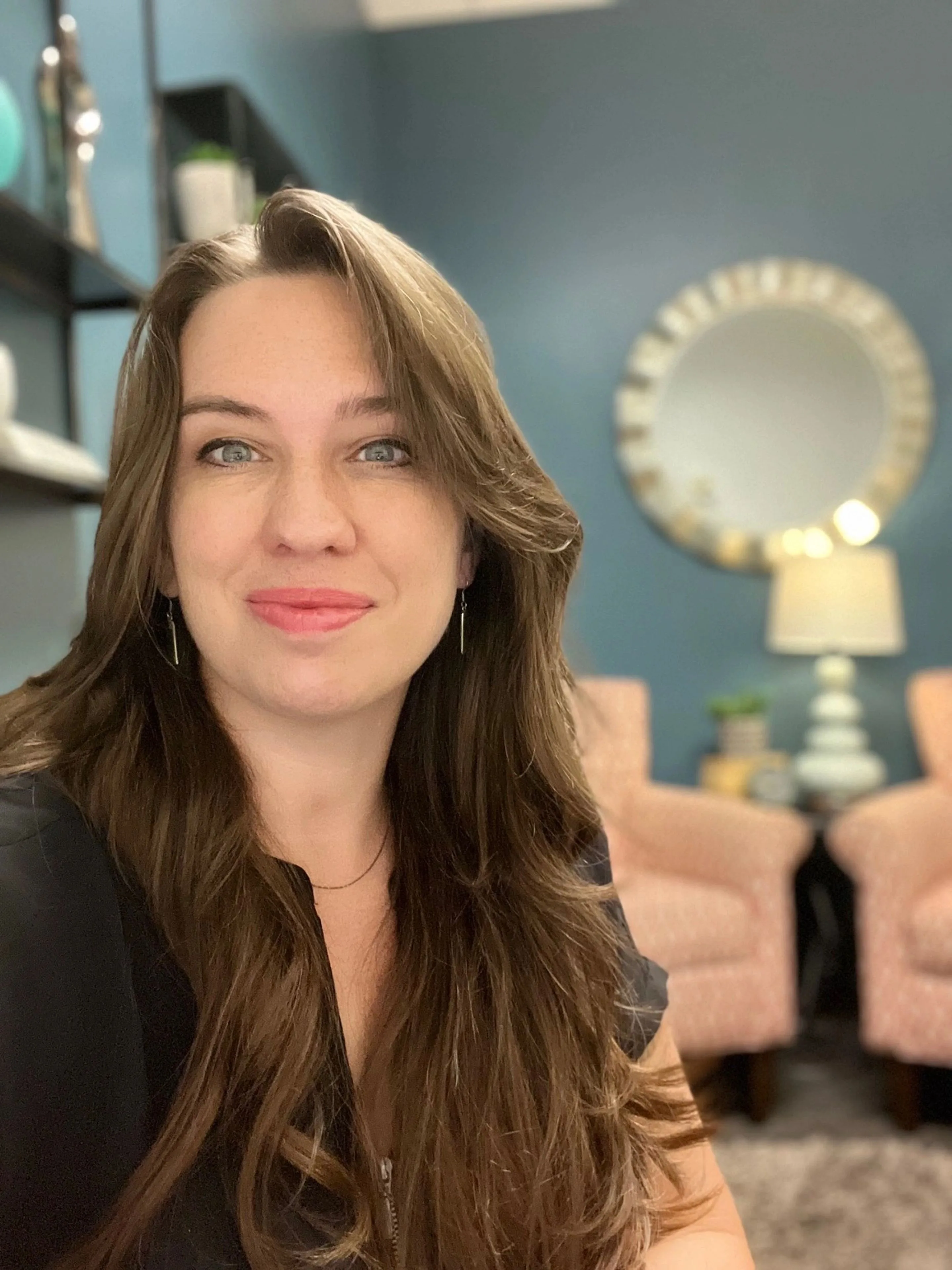 Hannah Sholar, life coach, smiling in an office with a round mirror behind her