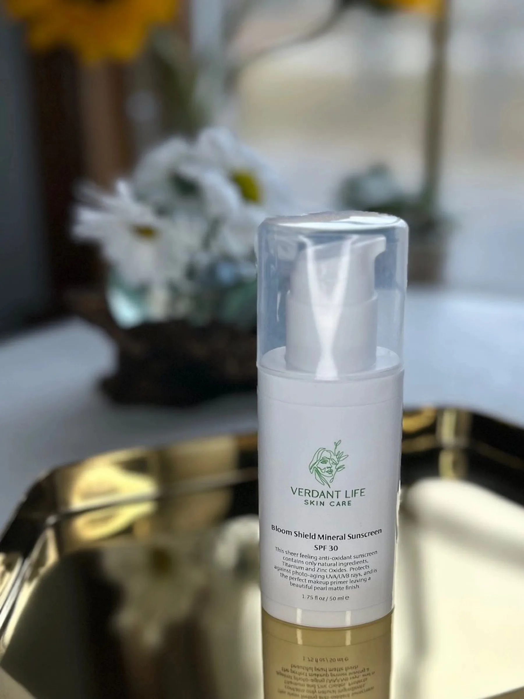 White pump bottle with a clear cap of Bloom Shield Mineral Sunscreen SPF 30 on a gold tray.