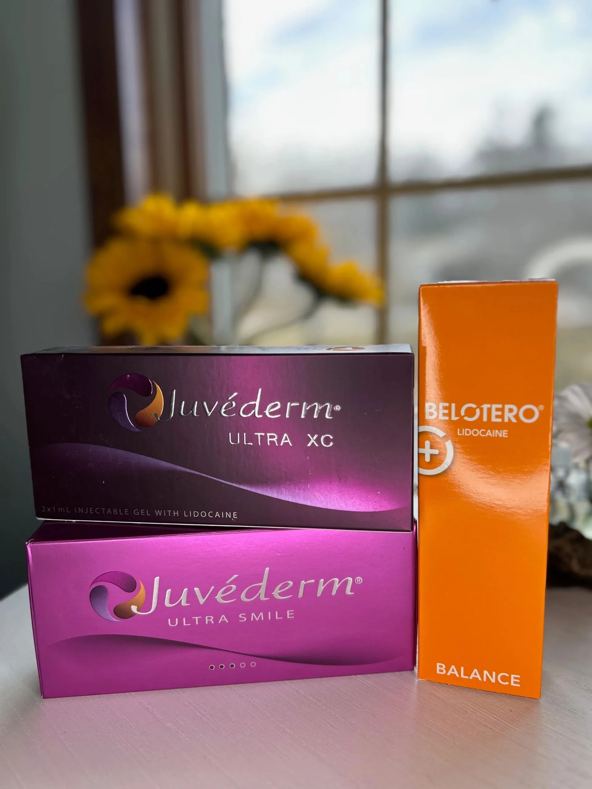 Boxes of Juvederm and Belotero dermal filler beside sunflowers