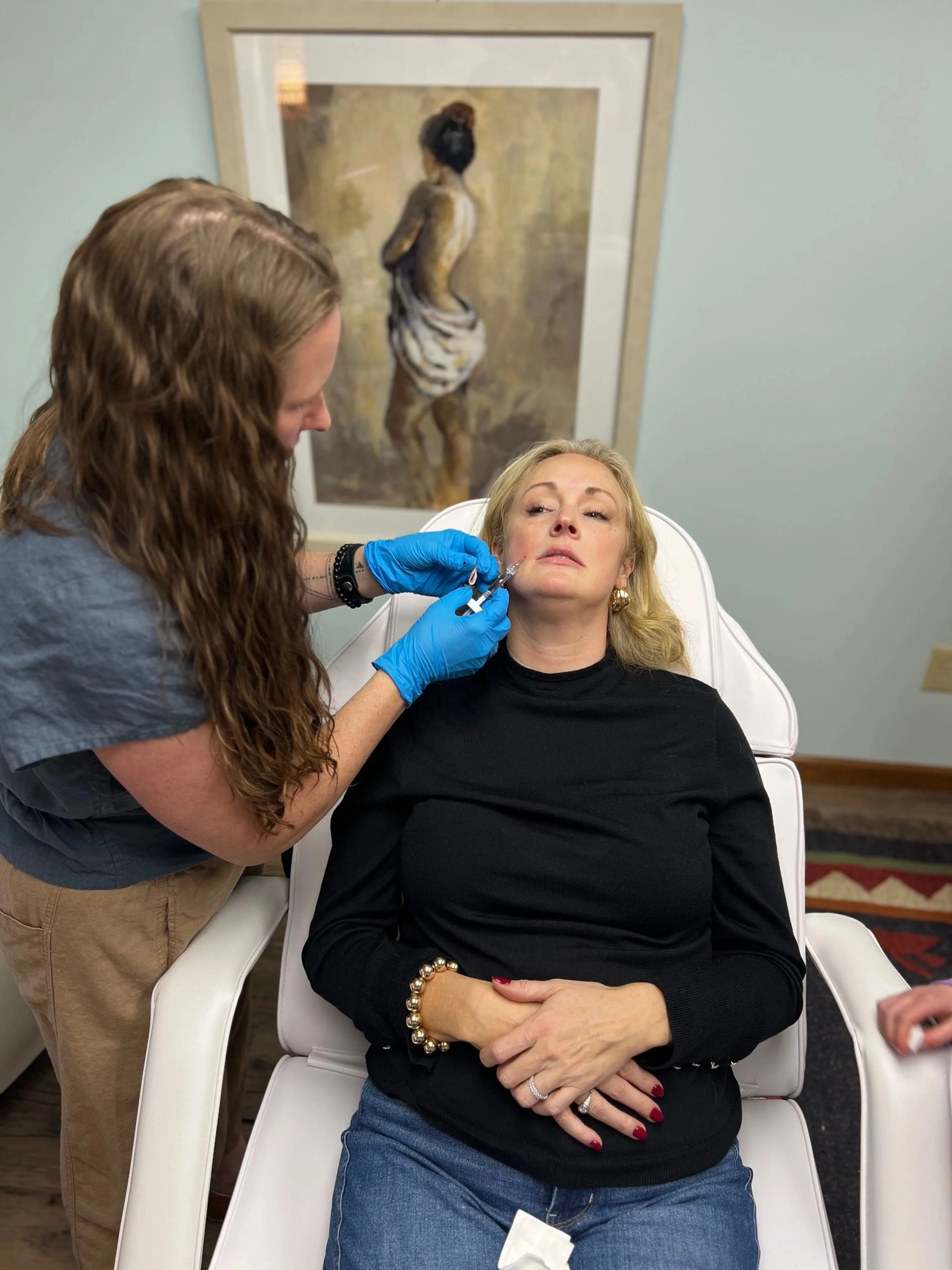 Provider in blue gloves giving an injection near a seated woman's mouth