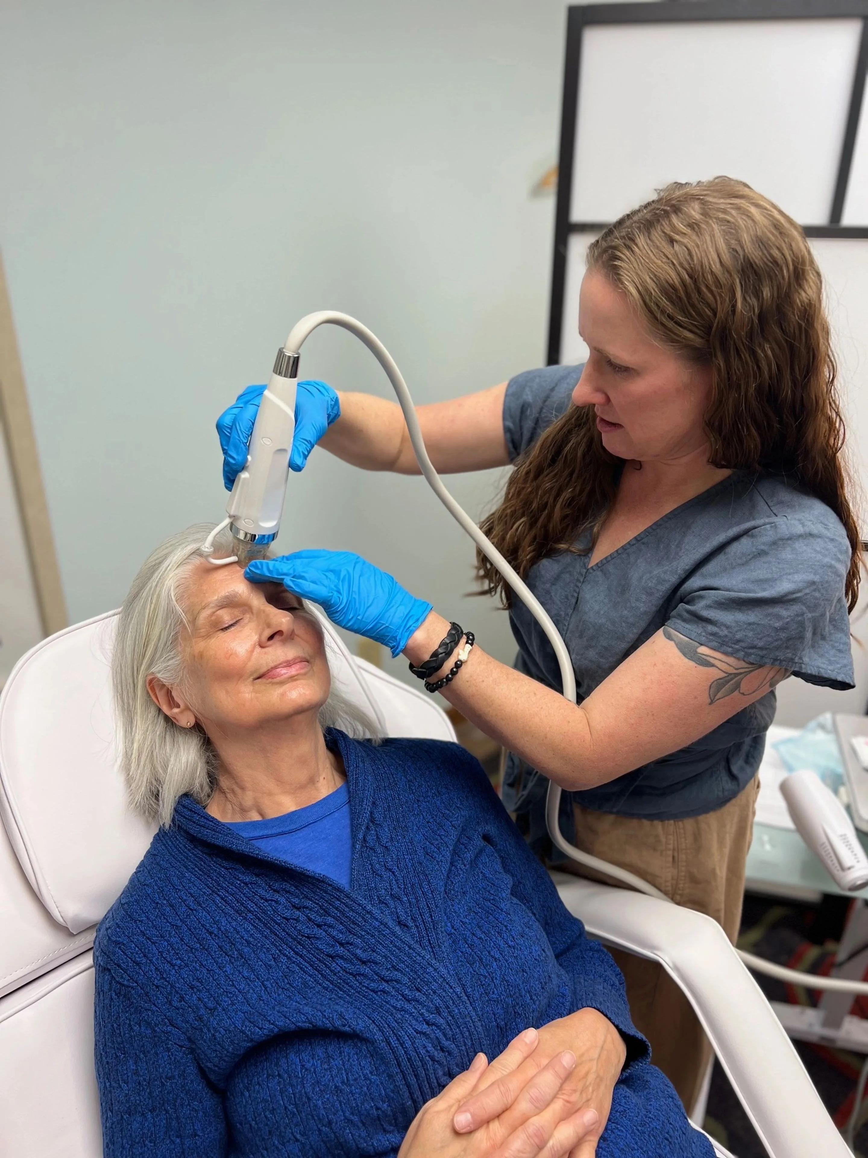Provider in blue gloves treating an older woman's forehead with a handheld device