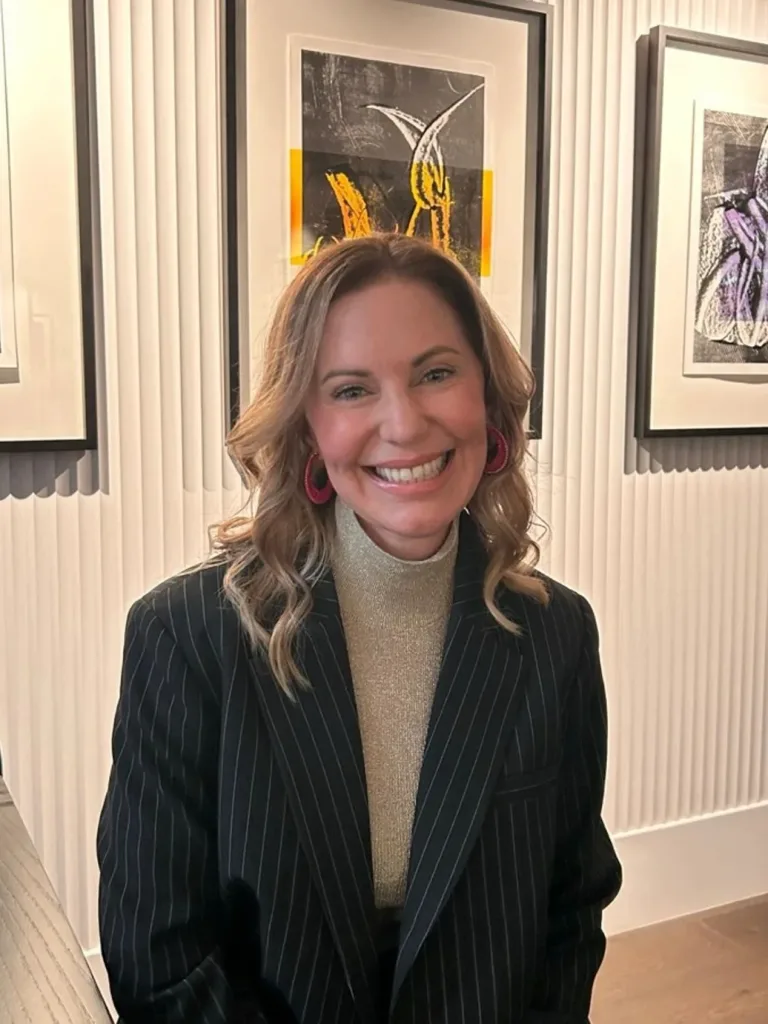 Smiling woman in a pinstripe blazer and gold top posing indoors.