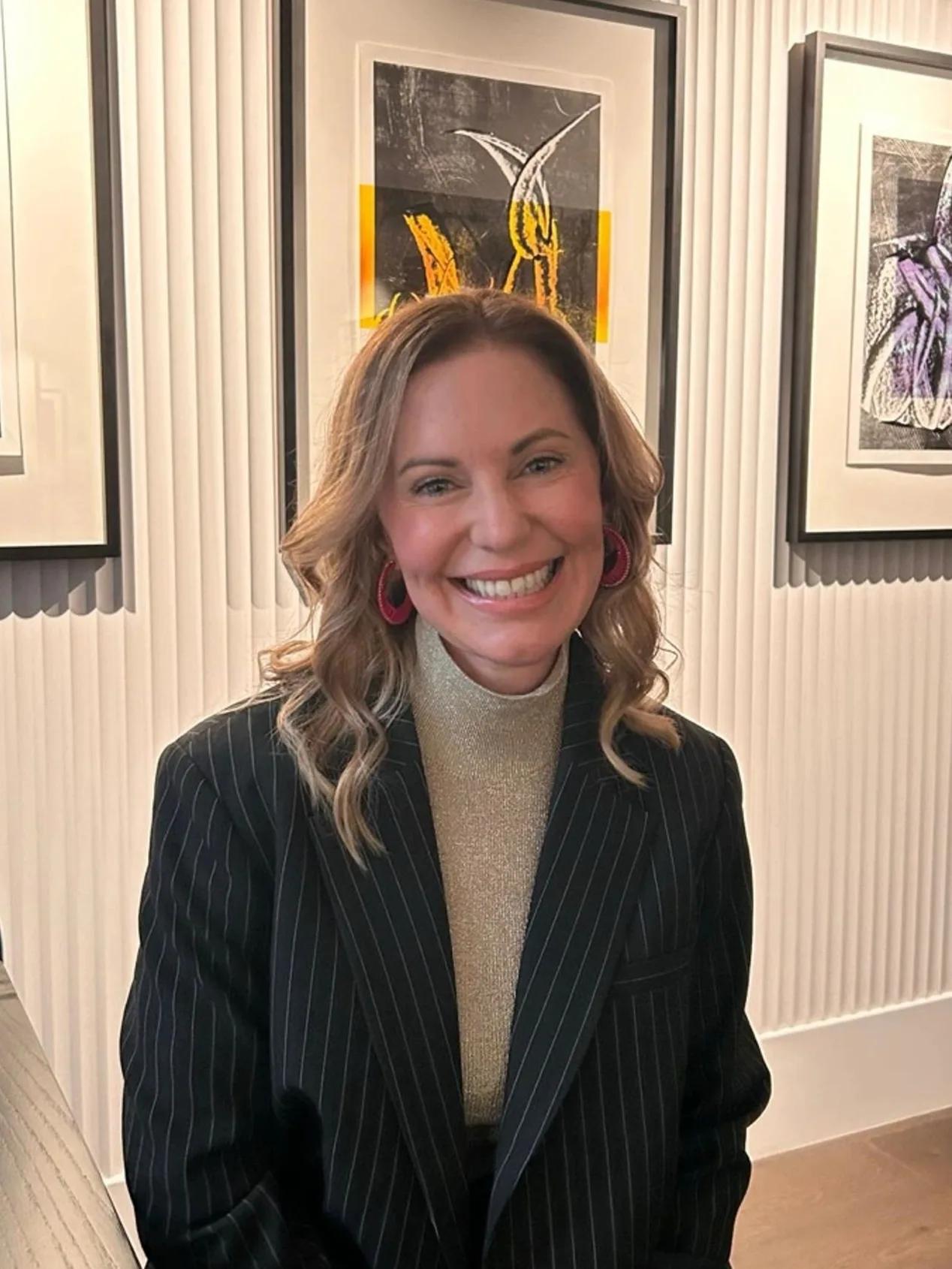 Smiling woman in a pinstripe blazer and gold top posing indoors.