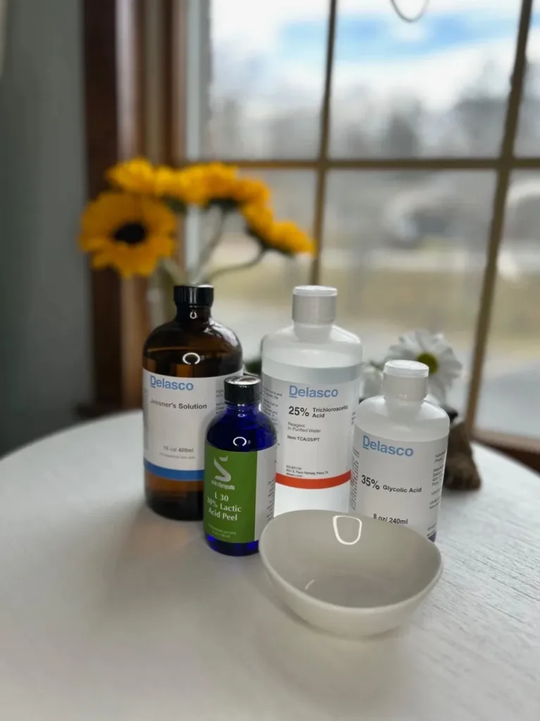 Peel solution bottles and a small white bowl on a round table, with sunflowers by a window.